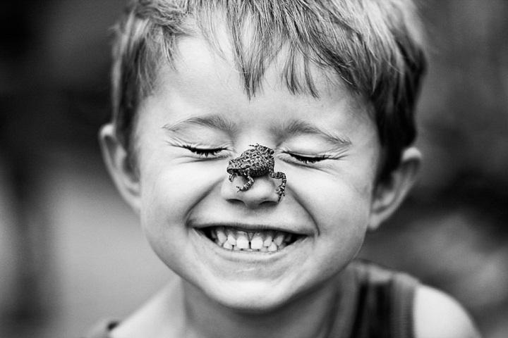 niño sonriendo con una rana sobre la nariz